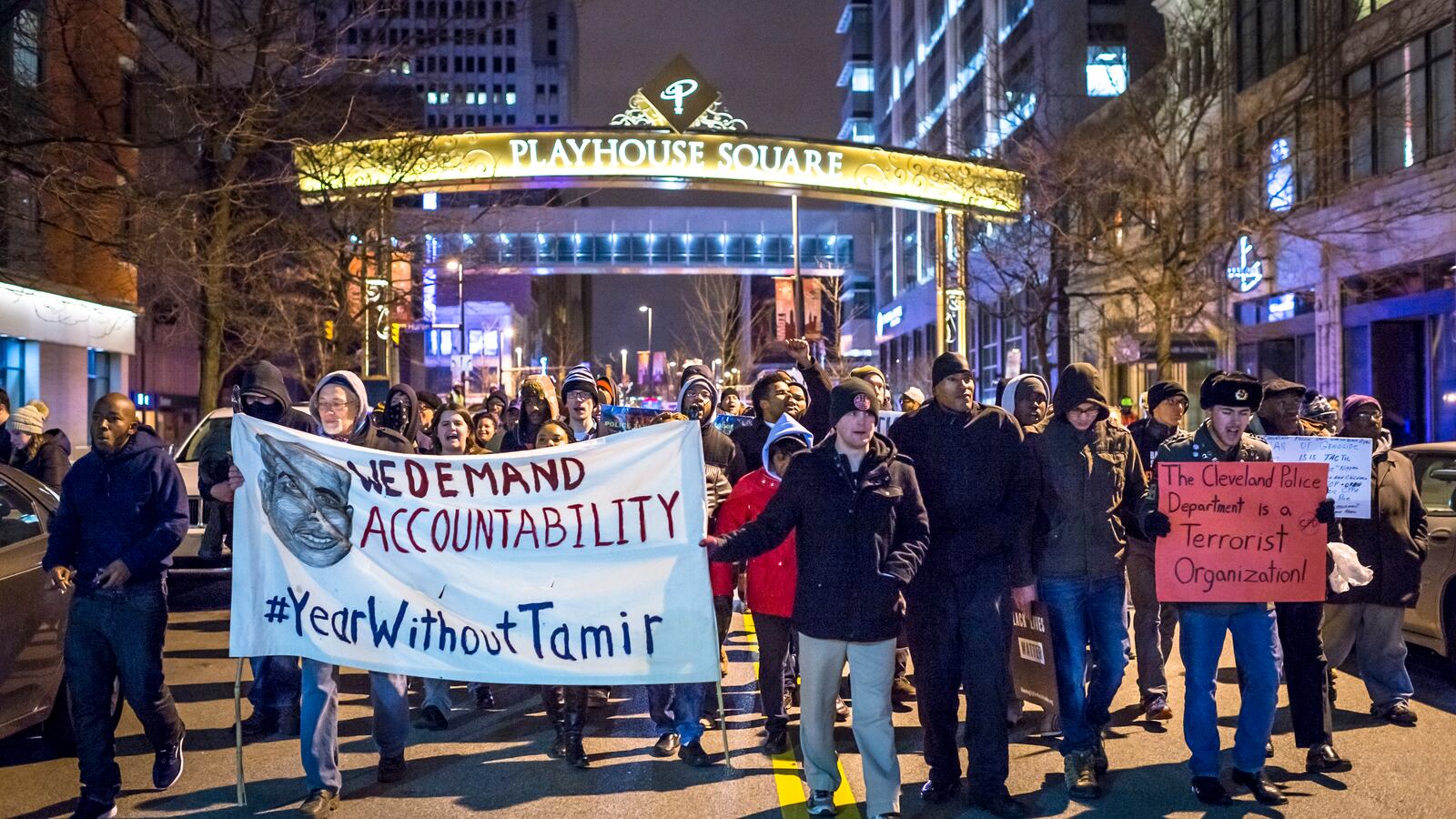 A group of protesters march downtown with a sign that reads, “We demand accountability. #YearWithoutTamir.”