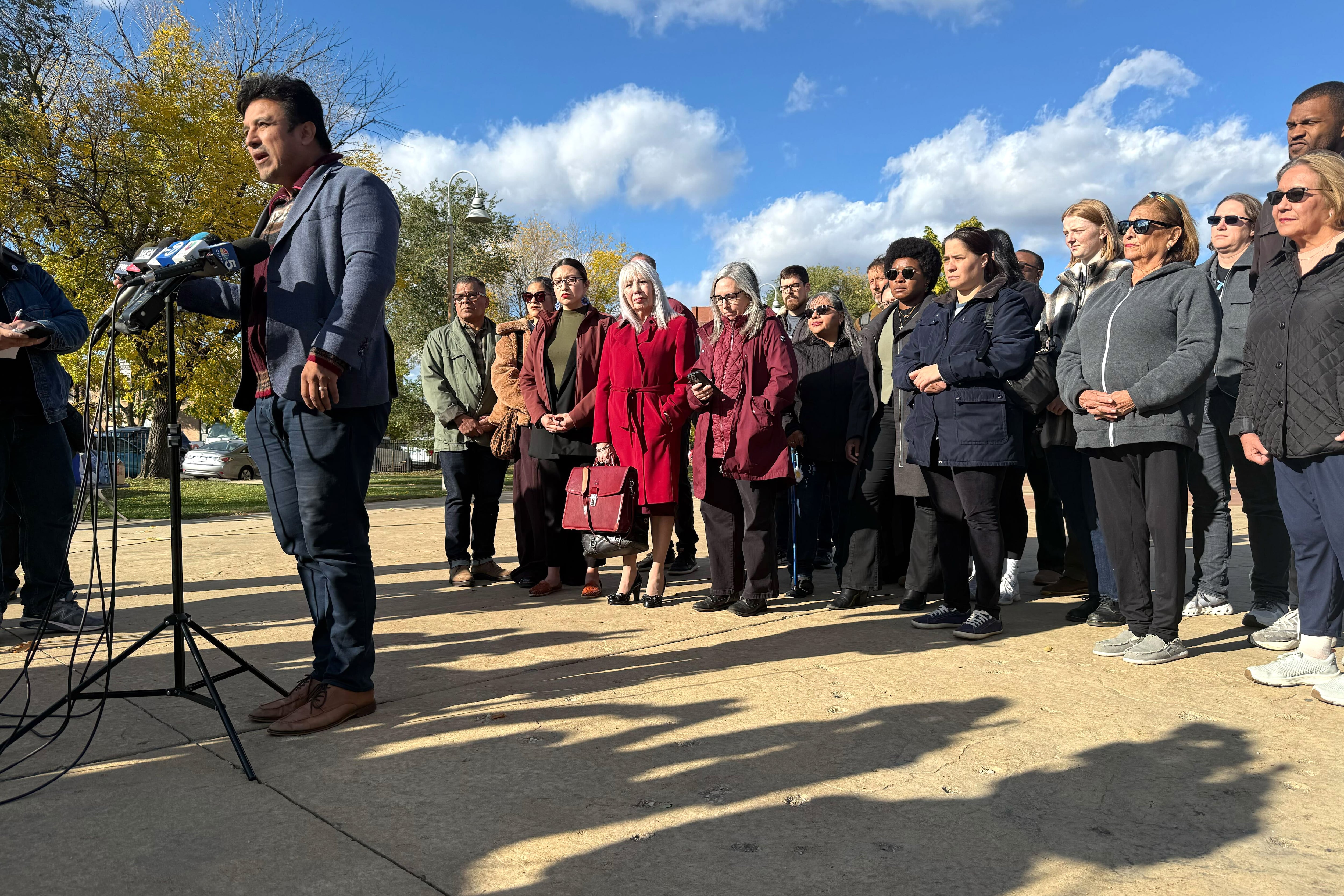 A man in a gray jacket speaks at a microphone.
