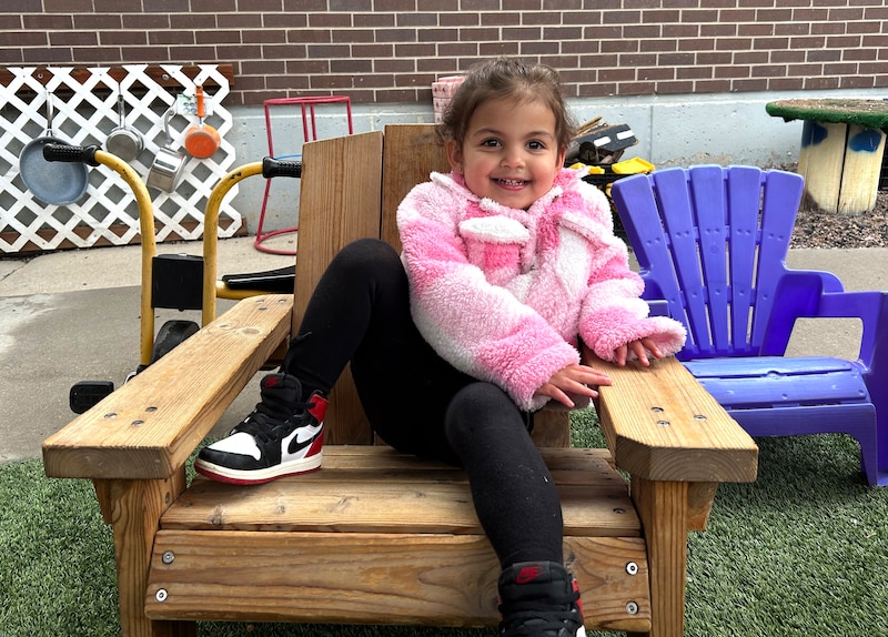 A little girl in pink sits in a chair.