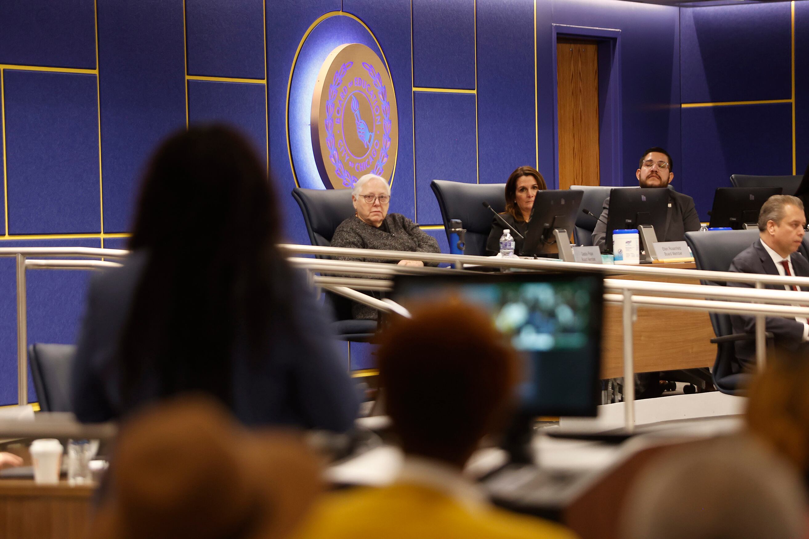 Four people in business attire sit at chairs in the background and a women in the foreground.