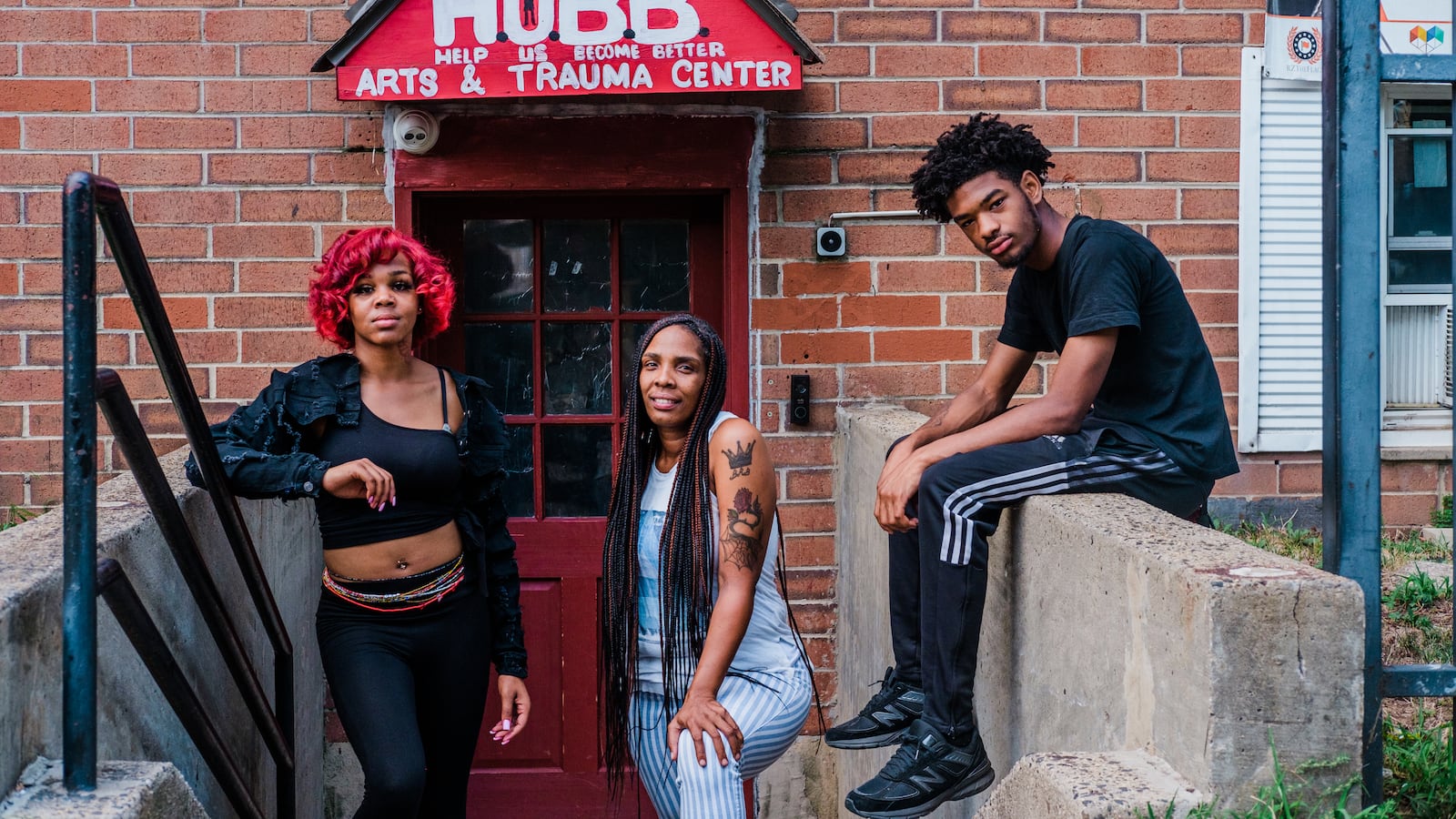 Three people pose in front of the entrance to HUBB on the stairwell of a brick building.