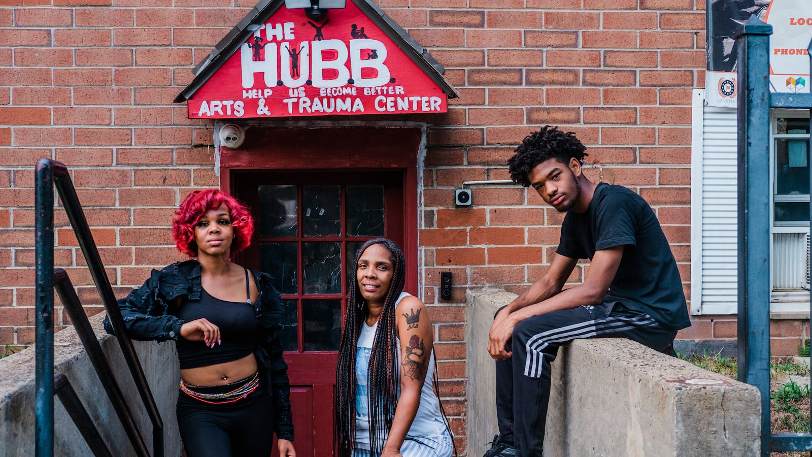 Three people pose in front of the entrance to HUBB on the stairwell of a brick building.