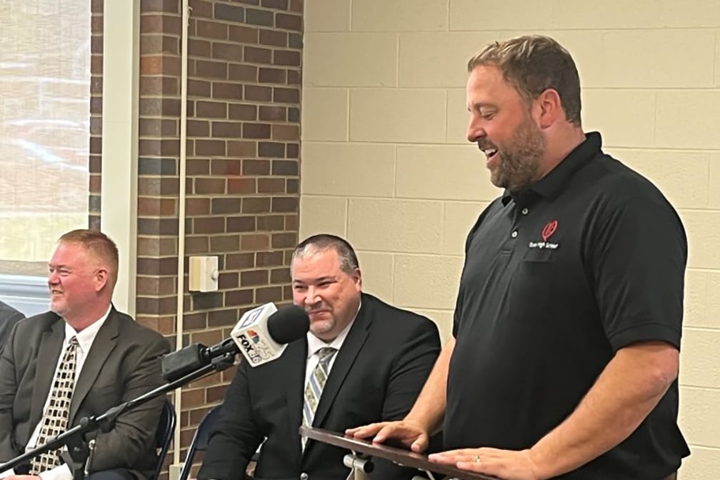 A man in a dark shirt stands at a podium.