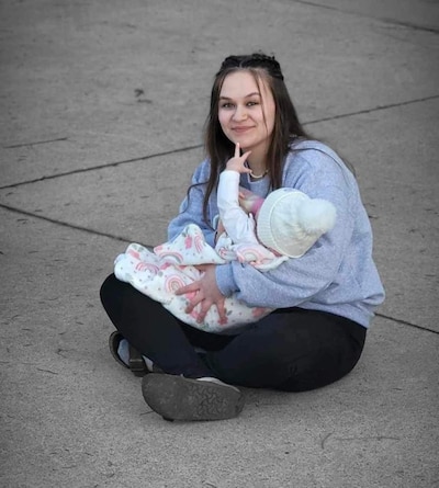 A young mother sits on the floor holding her baby daughter