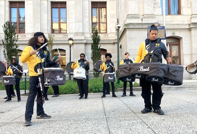Youth performers in yellow and black play music outside a building.