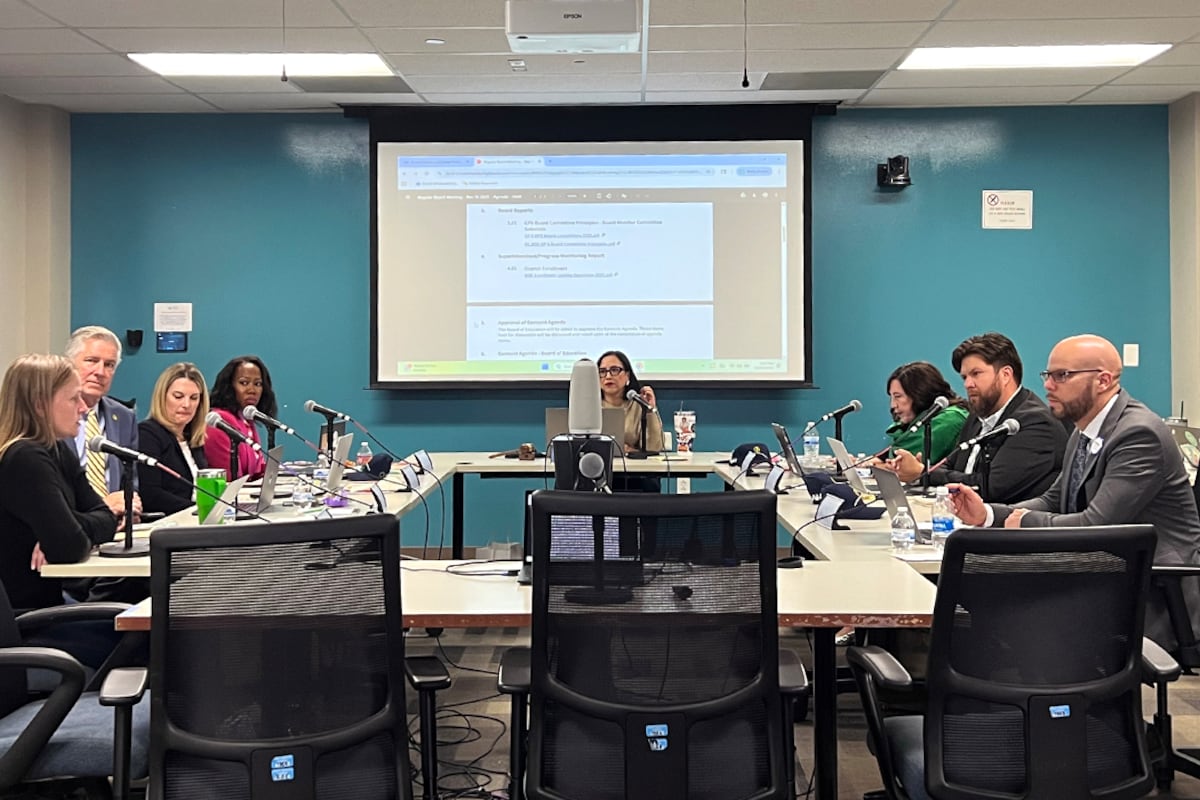 People in business attire are seated in a room with a teal colored wall.