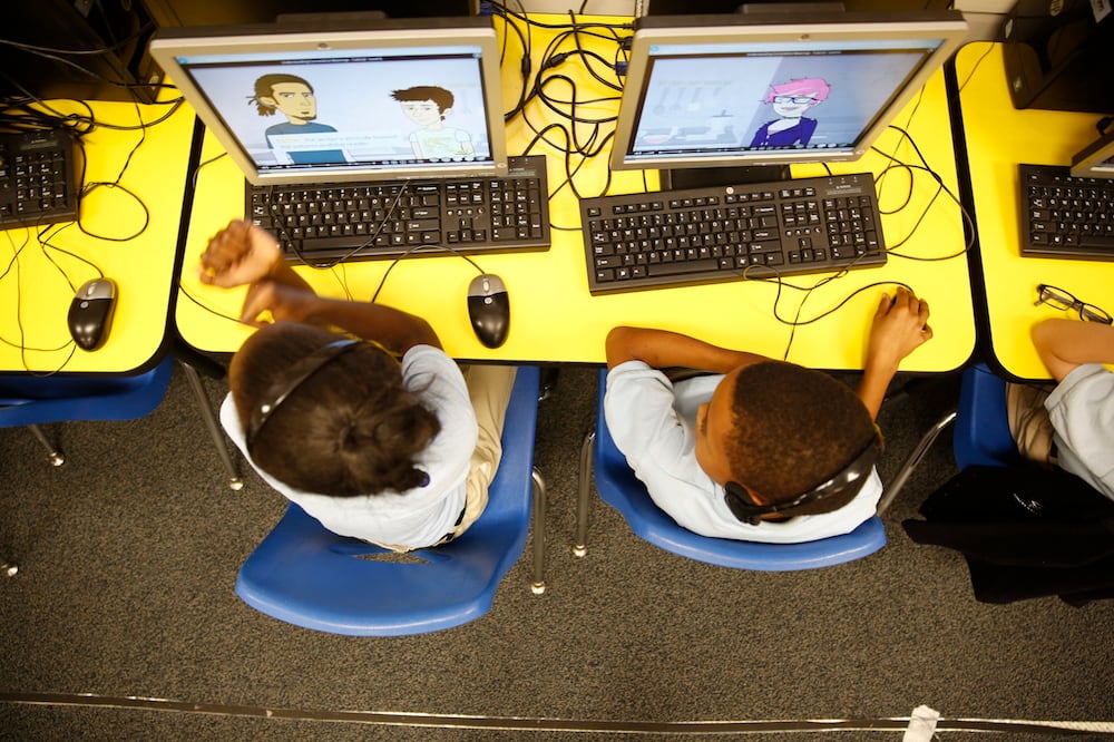 An aerial view of two young students working at computers in a classroom.