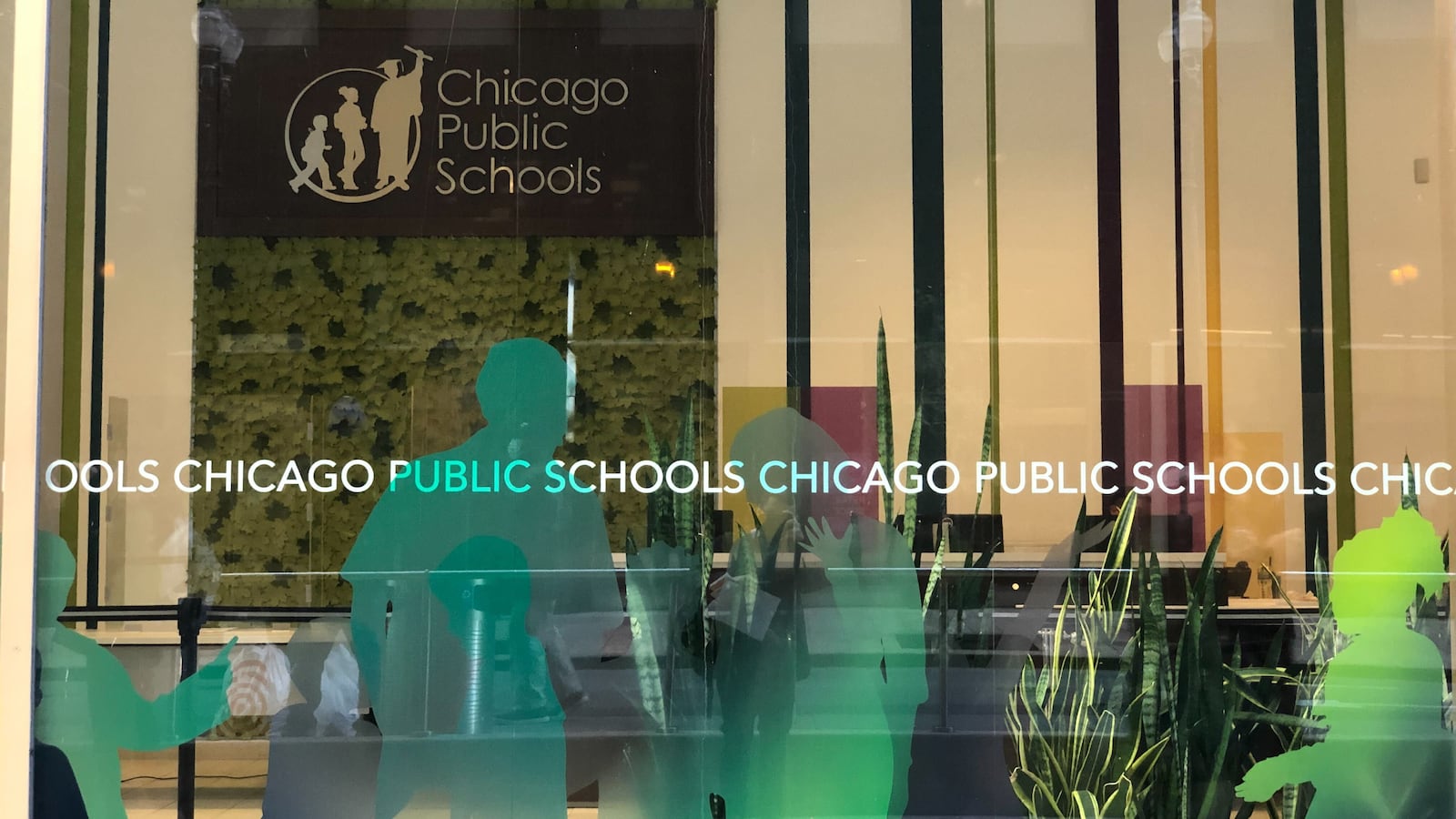 The facade of Chicago Public Schools headquarters, with the district’s sign hanging on the wall behind windows with green silhouettes of students.