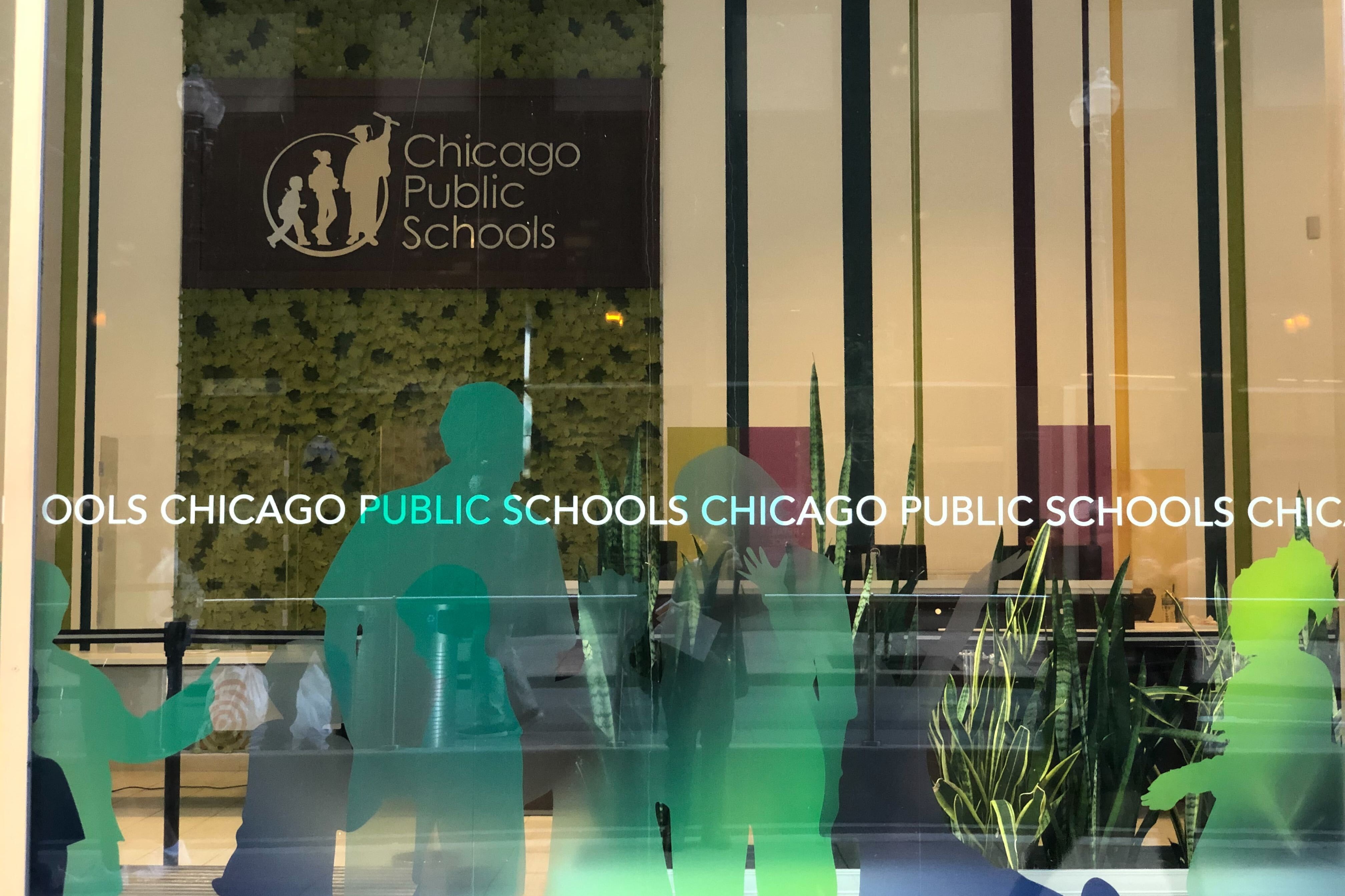 The facade of Chicago Public Schools headquarters, with the district’s sign hanging on the wall behind windows with green silhouettes of students.