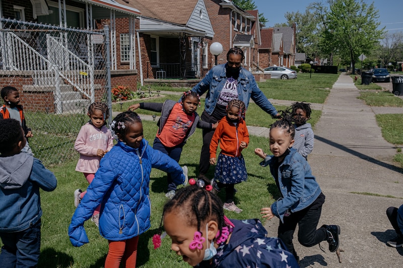A group of young students play outside while an adult watches.