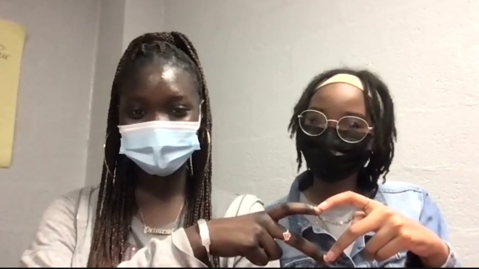 Two students wearing face masks make a heart sign with their hands.