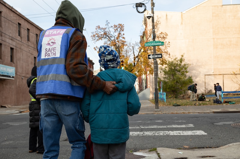 A man in a hoodie holds onto the jacket of a student.