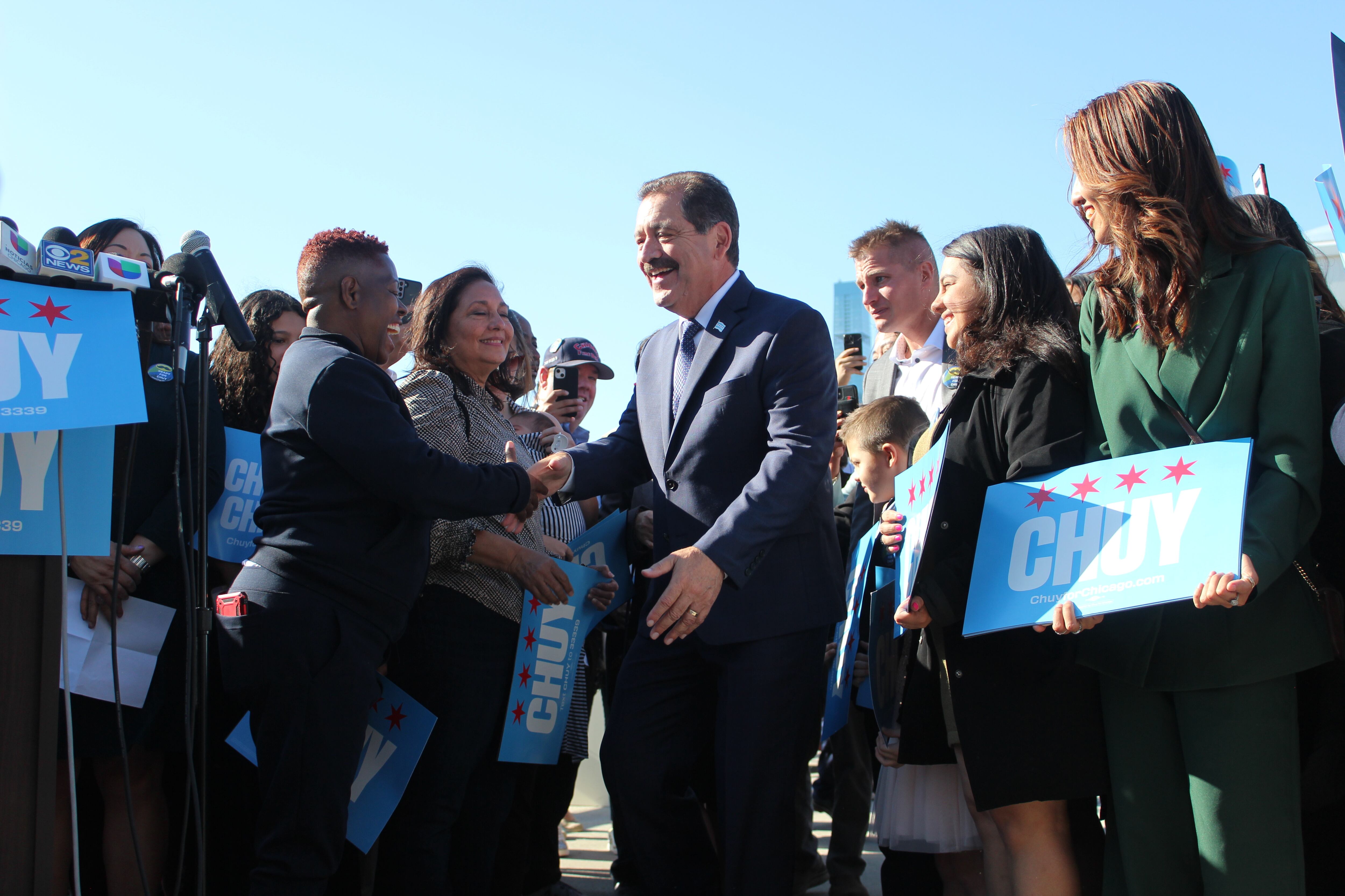 A politician walks through a crowd, shaking hands with supporters —some holding signs with his name.