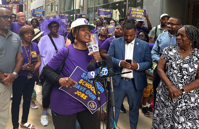 A woman in purple speaks surrounded by others.