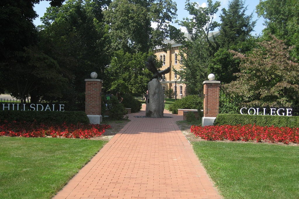 Open entrance gate to a college campus with bricked walkway that leads to a courtyard with a bronze statue of an eagle