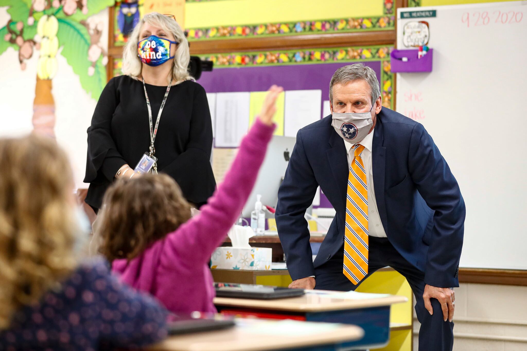 Gov. Bill Lee squats to talk to elementary students at the front of the classroom while students raise their hands.