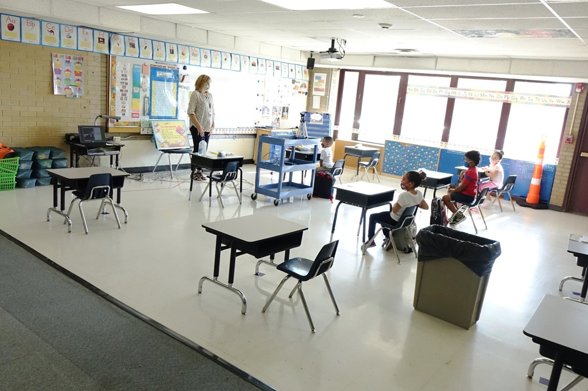 A school classroom with several students seated at desks and a teacher at the front of the room.