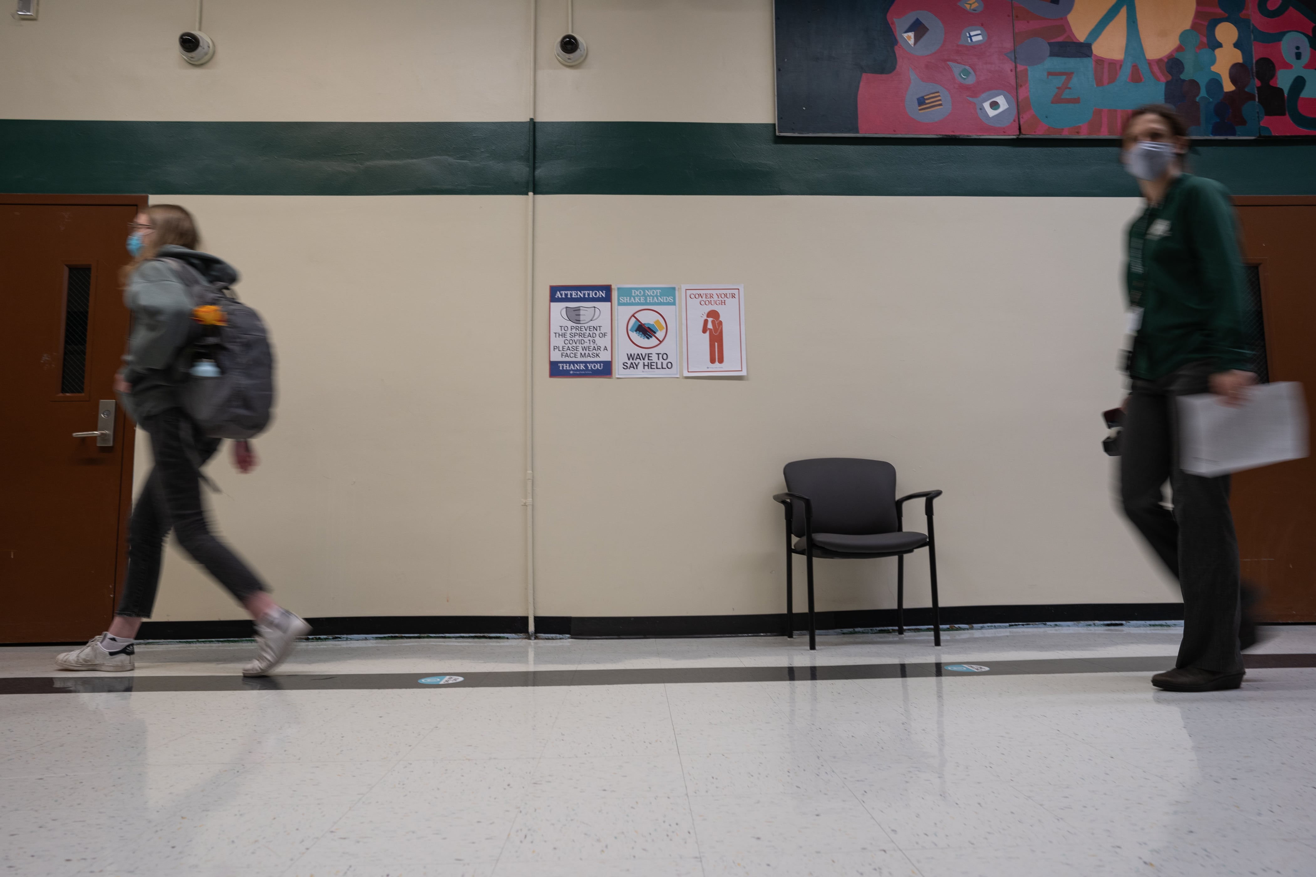 Students and staff walk the halls of Senn High School, past a poster showing COVID-19 safety guidelines, on the first week back to classrooms on April 23, 2021.