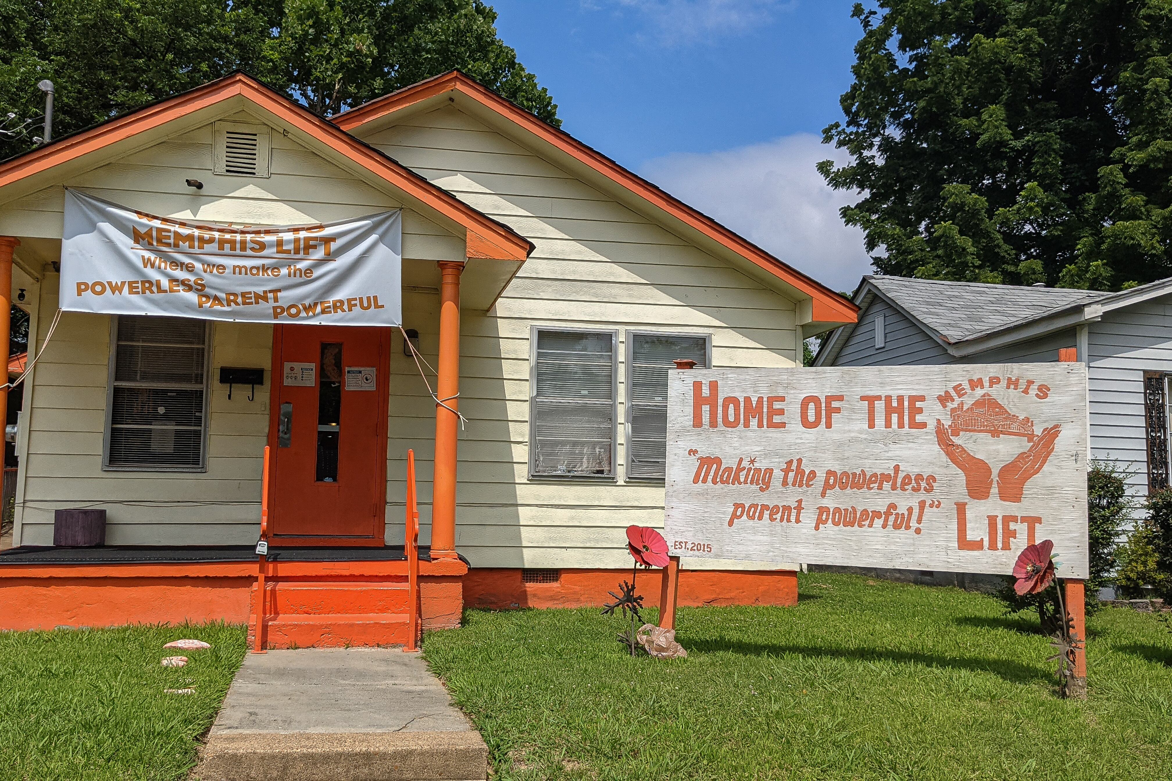 An orange and white home sits in a North Memphis neighborhood with a sign in front of it that says, “Home of The Memphis Lift: Making the powerless parent powerful!”