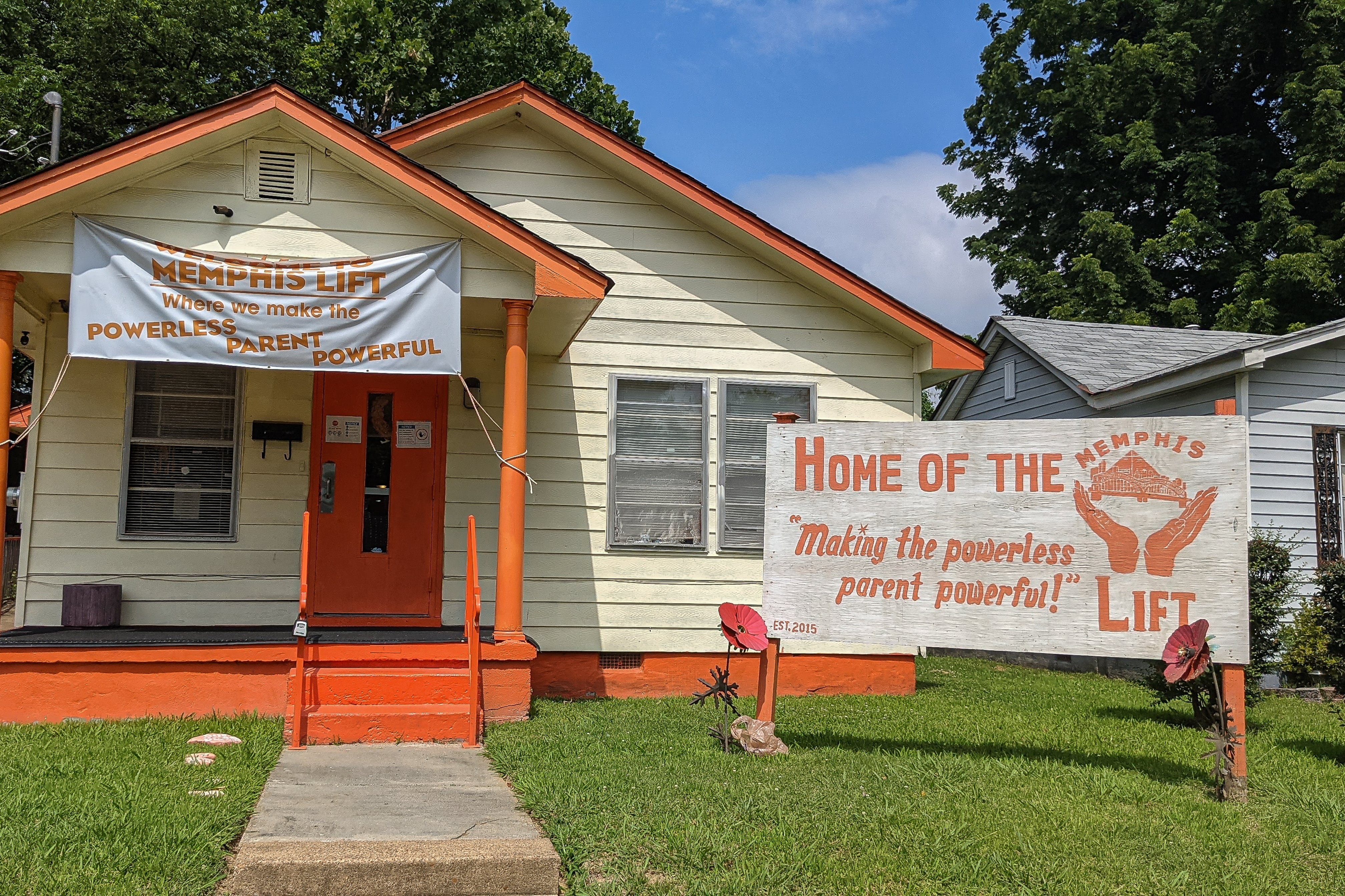 An orange and white home sits in a North Memphis neighborhood with a sign in front of it that says, “Home of The Memphis Lift: Making the powerless parent powerful!”