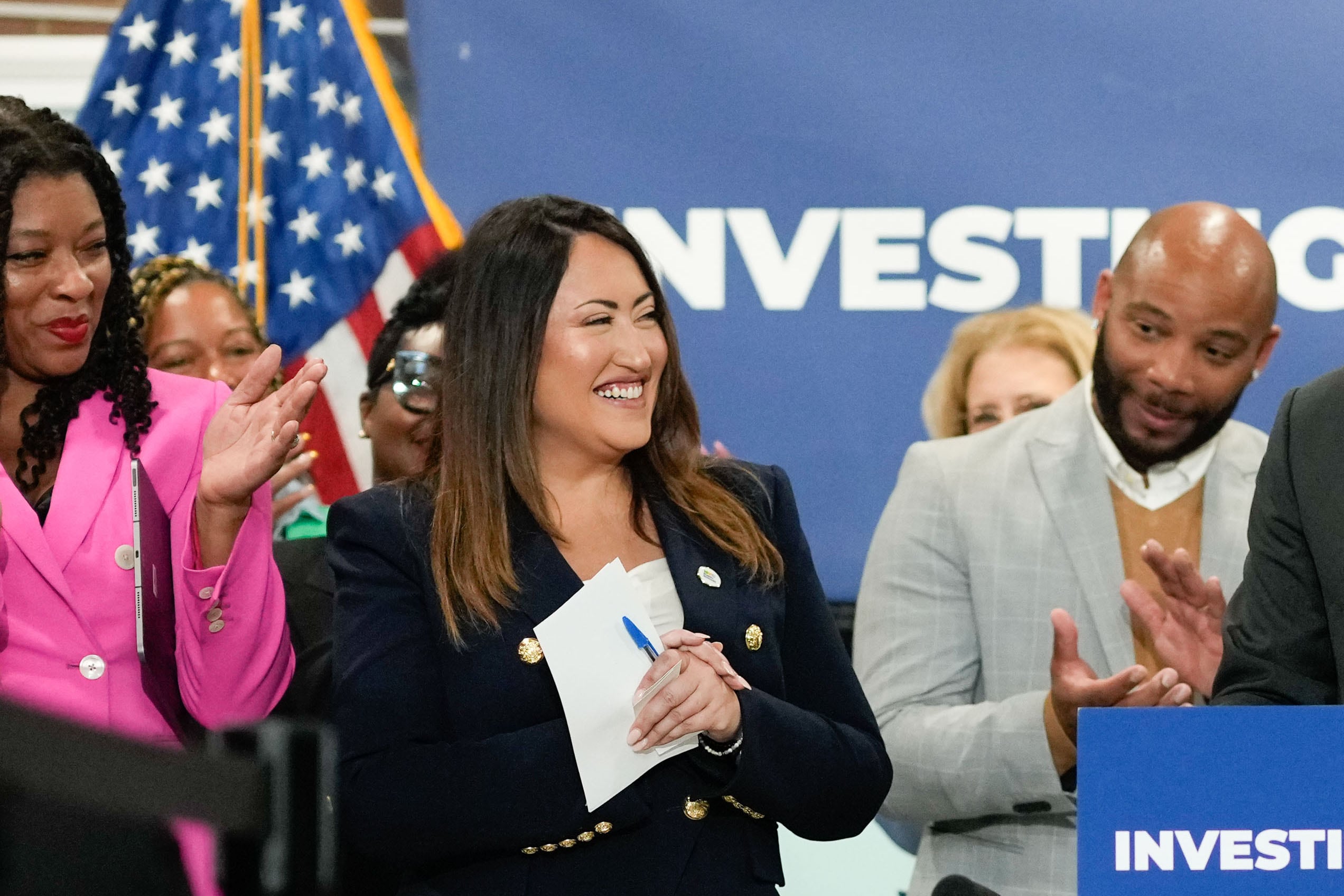 two women wearing suits stand in front of a group of people.