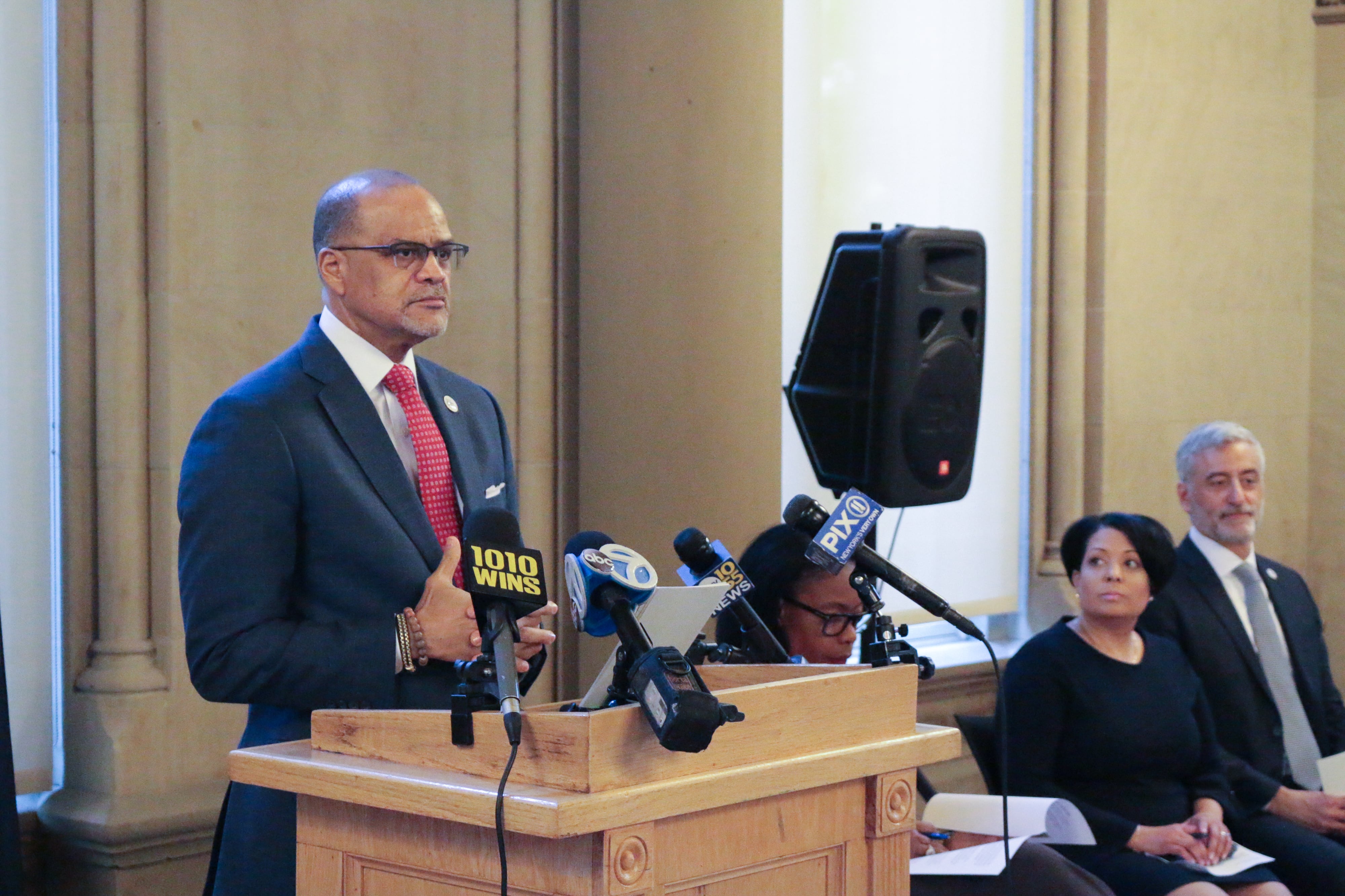 A man in a suit and a red tie stands at a lectern