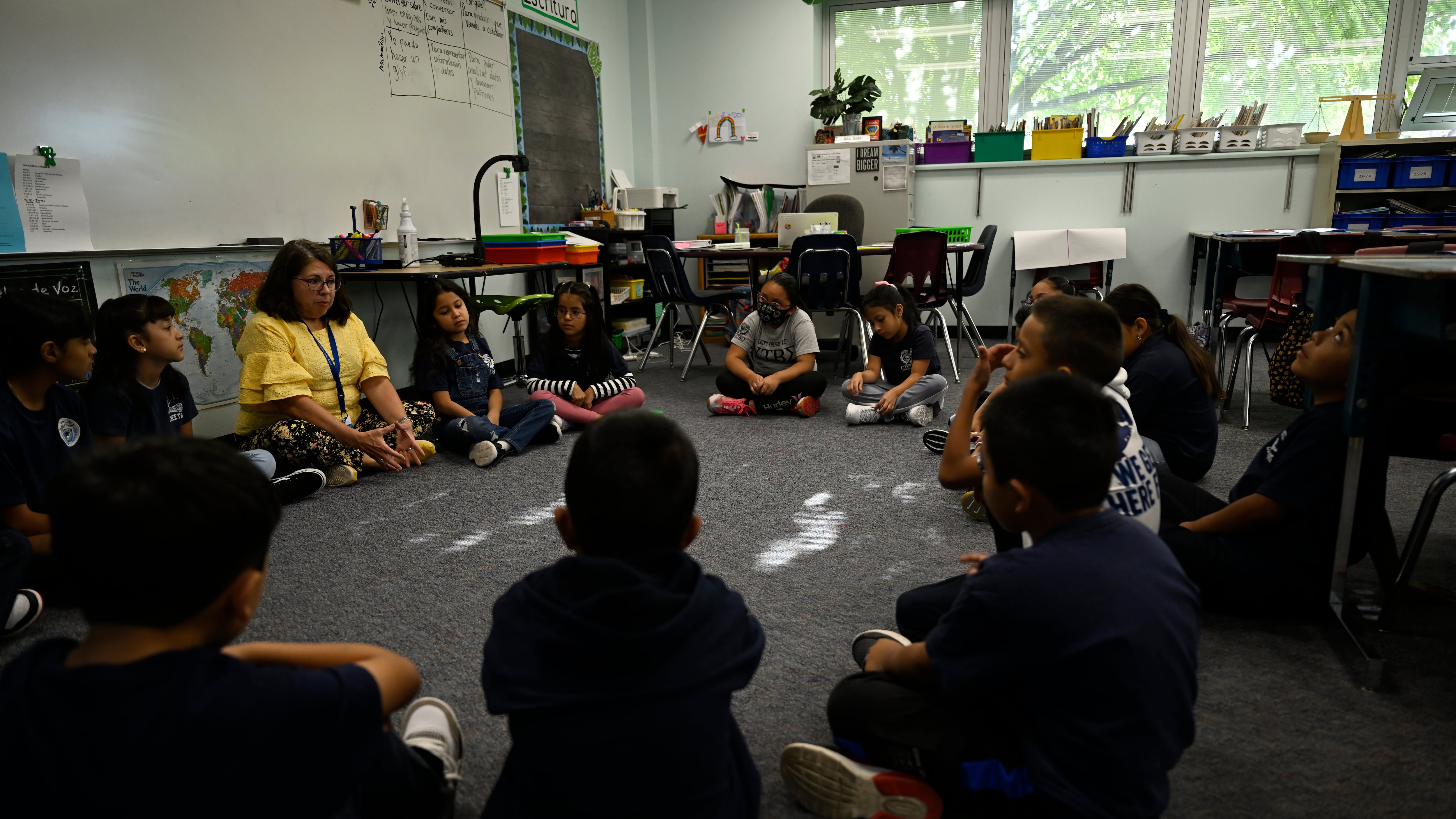 Elementary students sit on the carpet in a circle.
