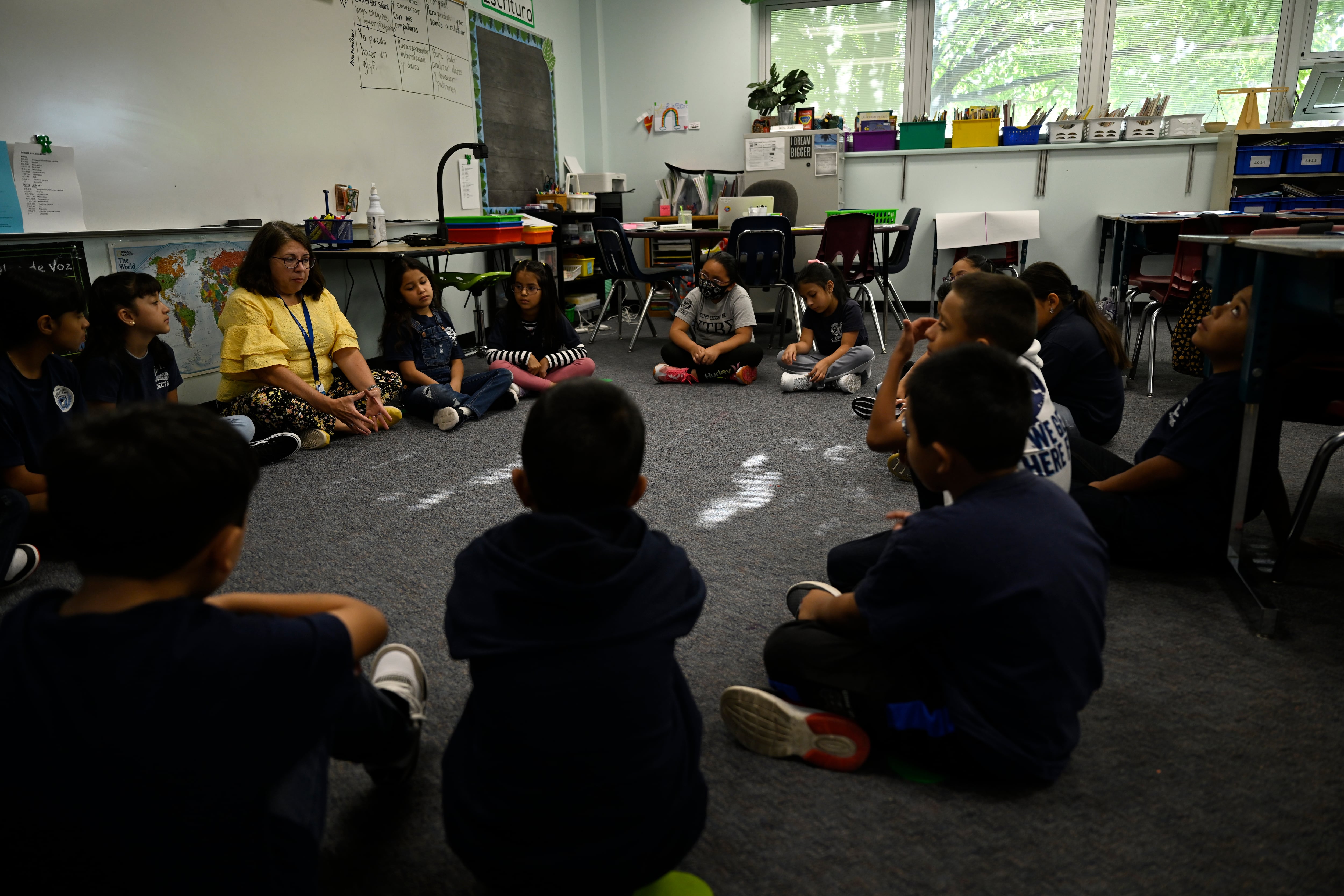 Elementary students sit on the carpet in a circle.
