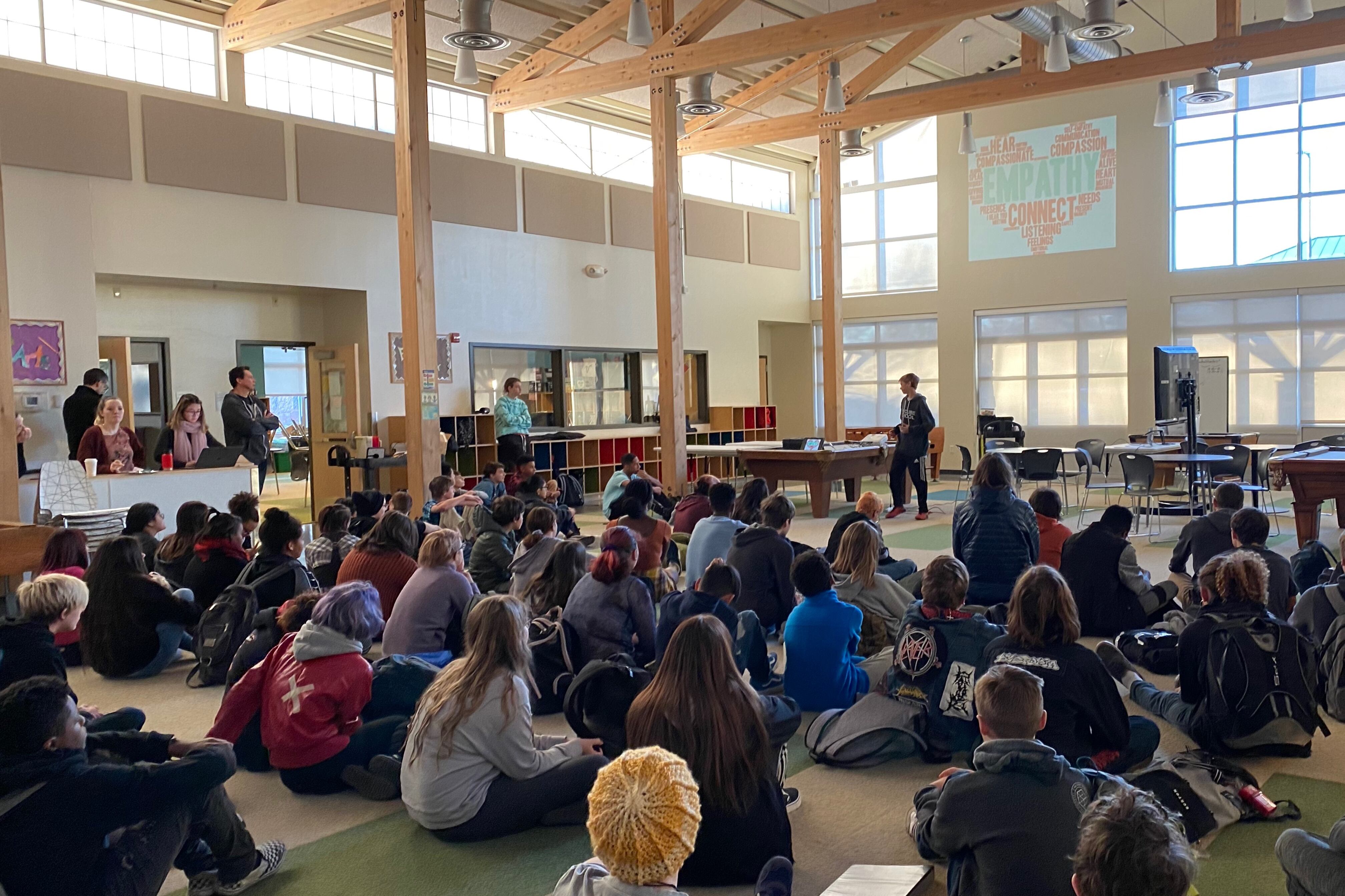 High school students sit on the floor in a large auditorium.