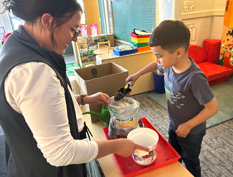 A woman with a white top and dark vest works with a young male student in a gray t-shirt.
