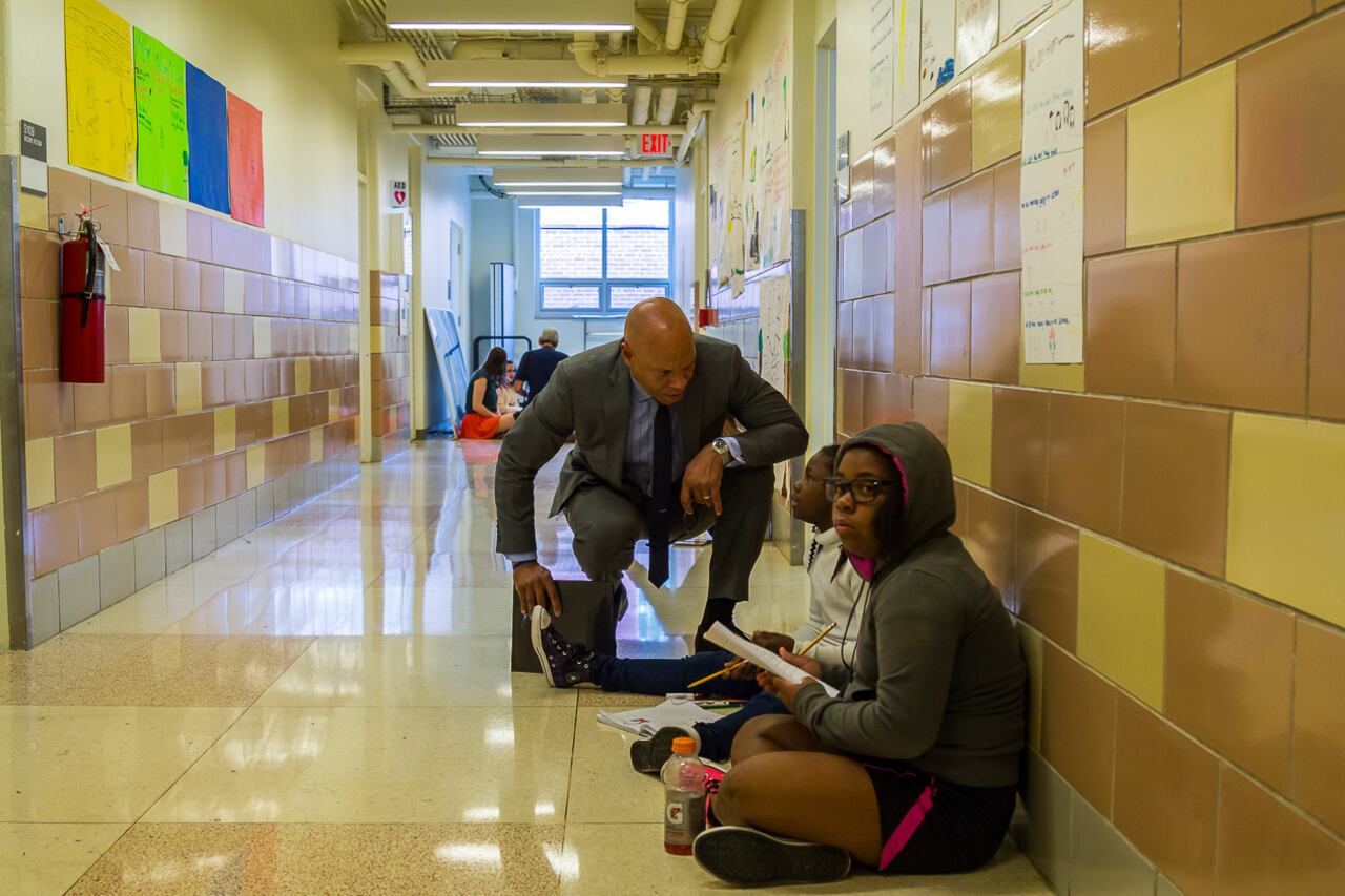 Philadelphia Superintendent William Hite crouches down next to students in a hallway at Science Leadership Academy.