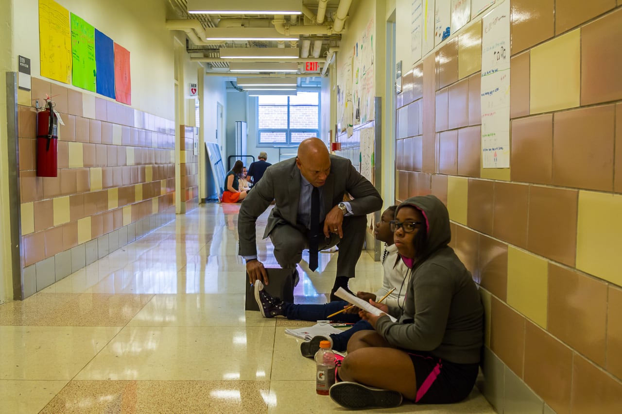 Philadelphia Superintendent William Hite crouches down next to students in a hallway at Science Leadership Academy.