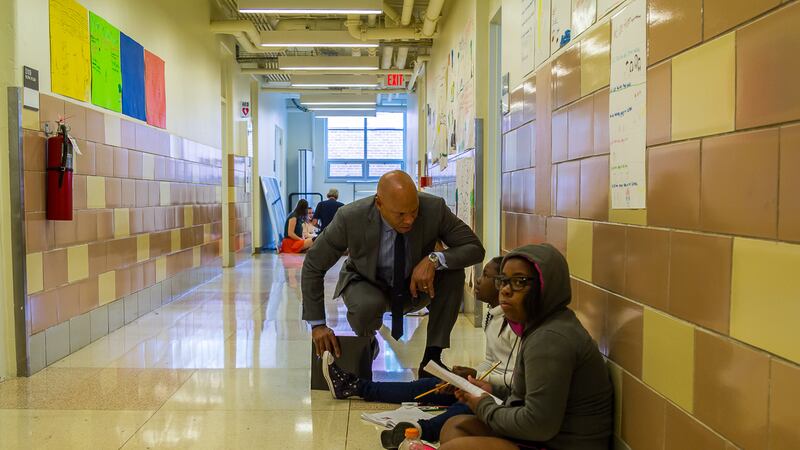 Philadelphia Superintendent William Hite crouches down next to students in a hallway at Science Leadership Academy.