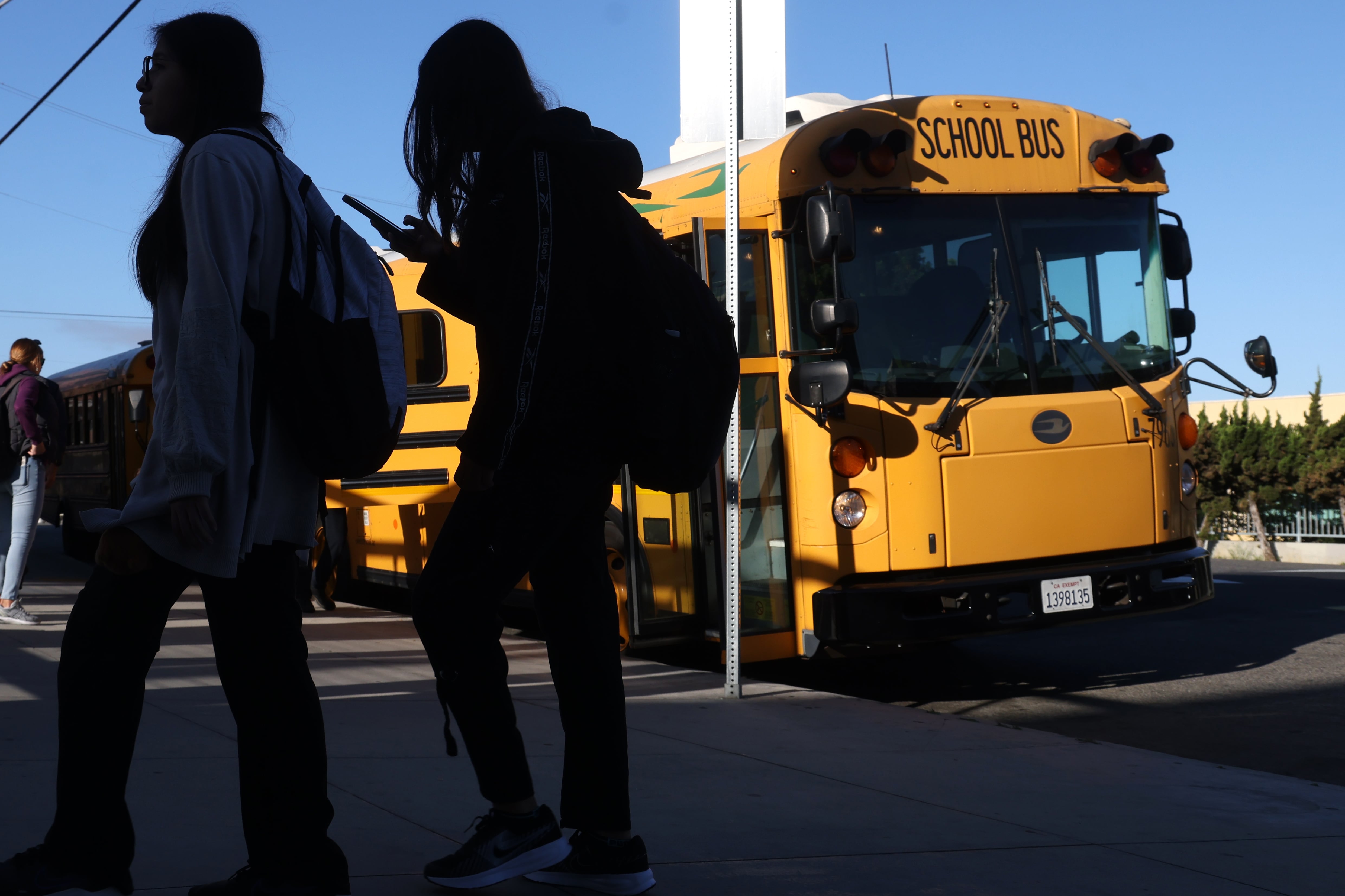 Students are silhouetted walking in front of a school bus.