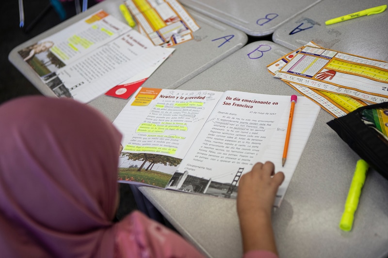 A female's student's hand is on an open book on a table.