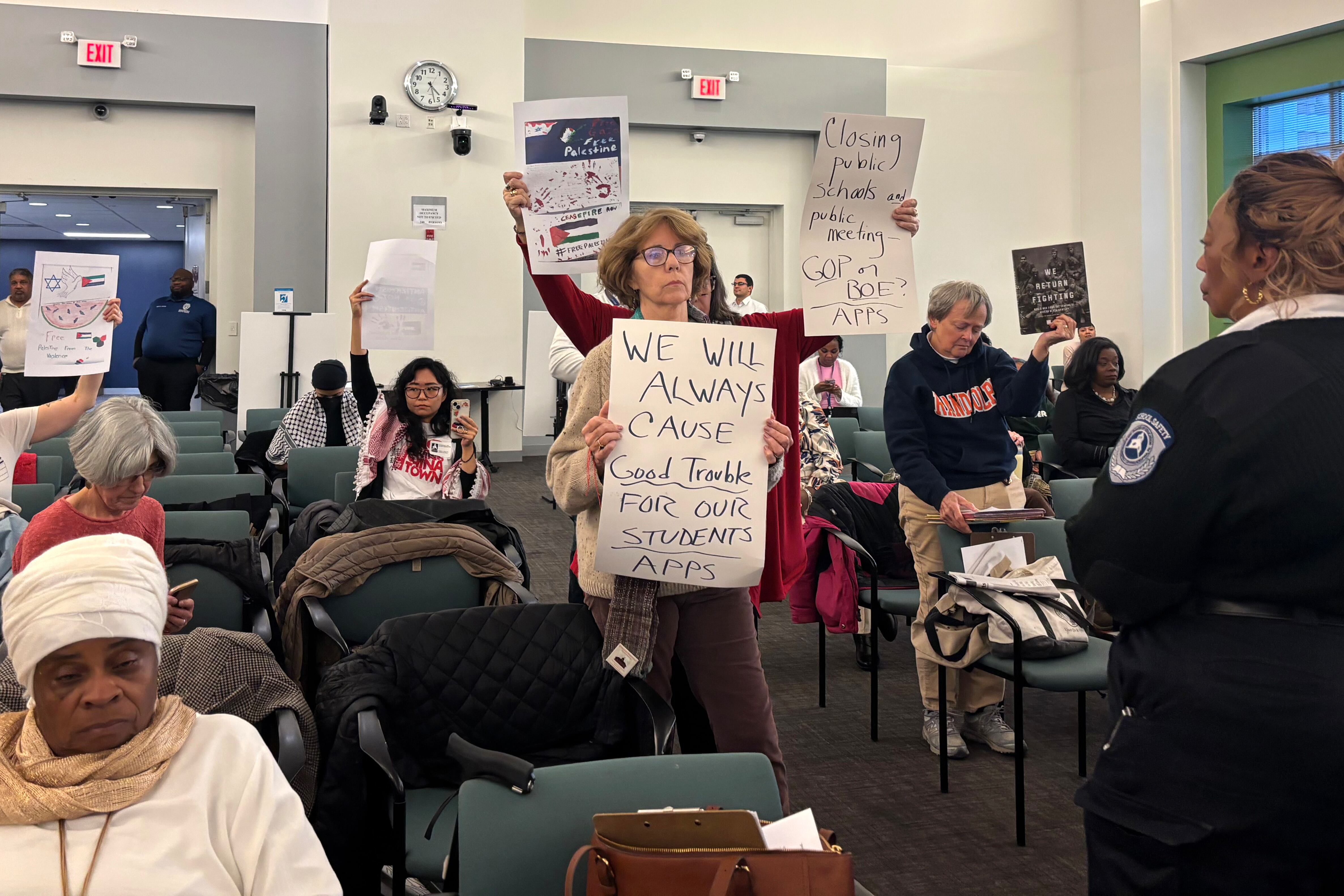 People hold signs at a meeting.