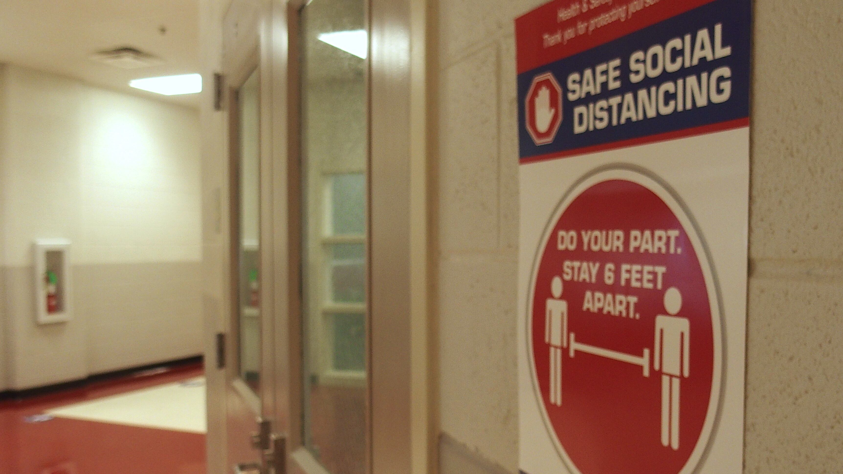 A poster promoting social distancing hangs in a school building hallway