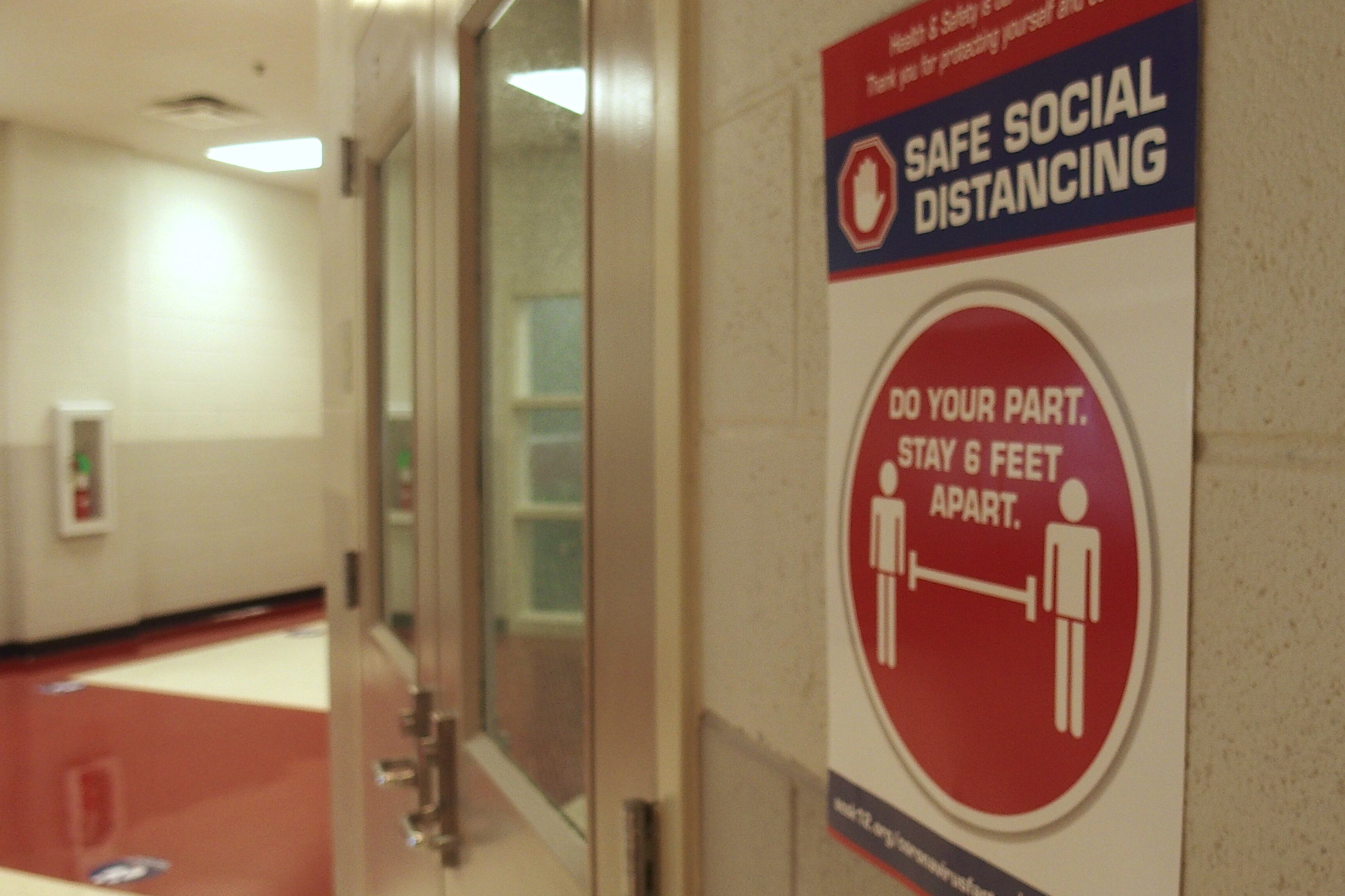 A poster promoting social distancing hangs in a school building hallway