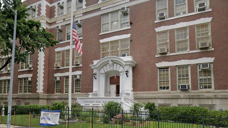 A brown brick building with a white entrance and an American flag in the foreground.