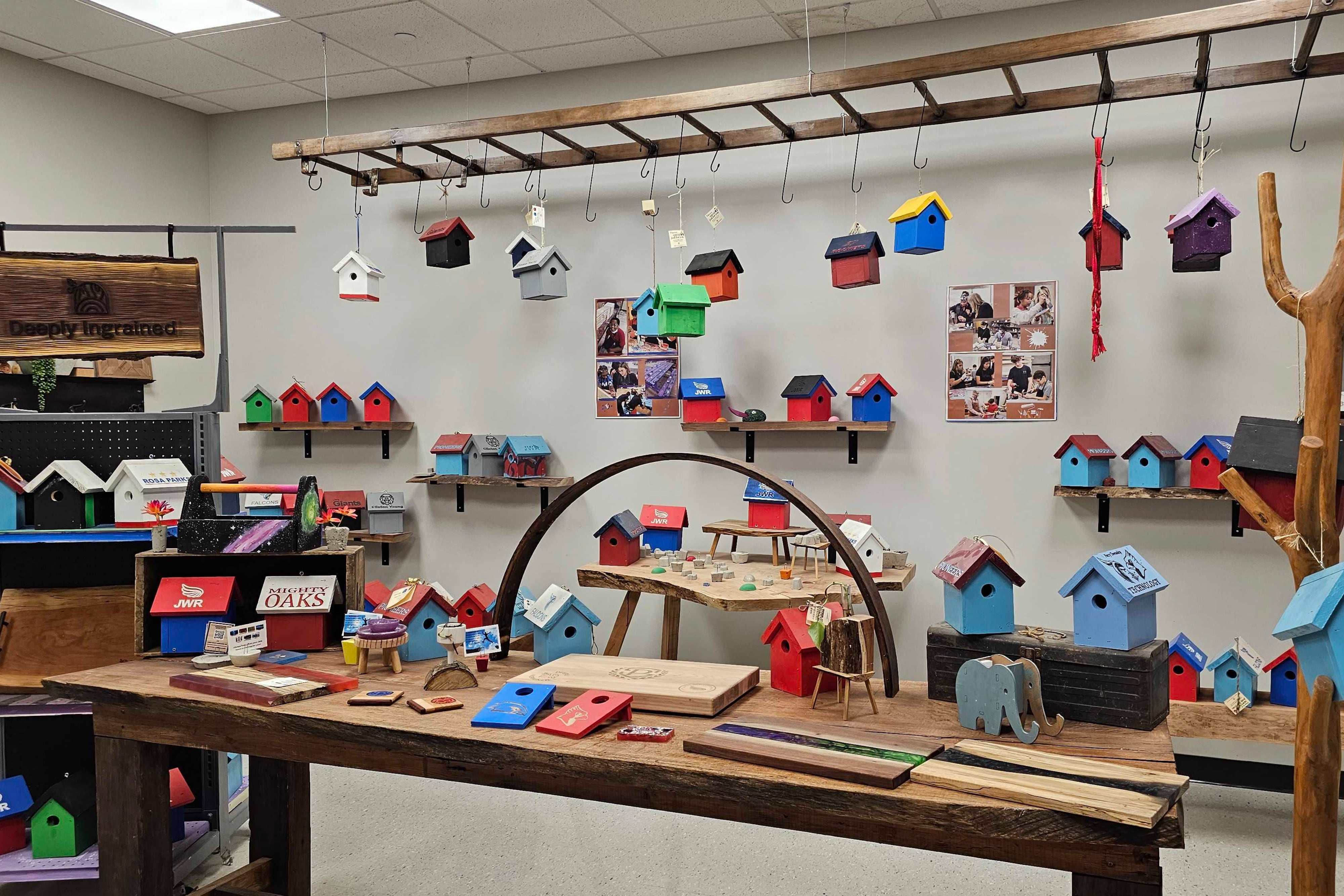 Dozens of multicolored birdhouses are hanging from the ceiling and displayed on shelves and counter space inside of a middle school's woodshop.