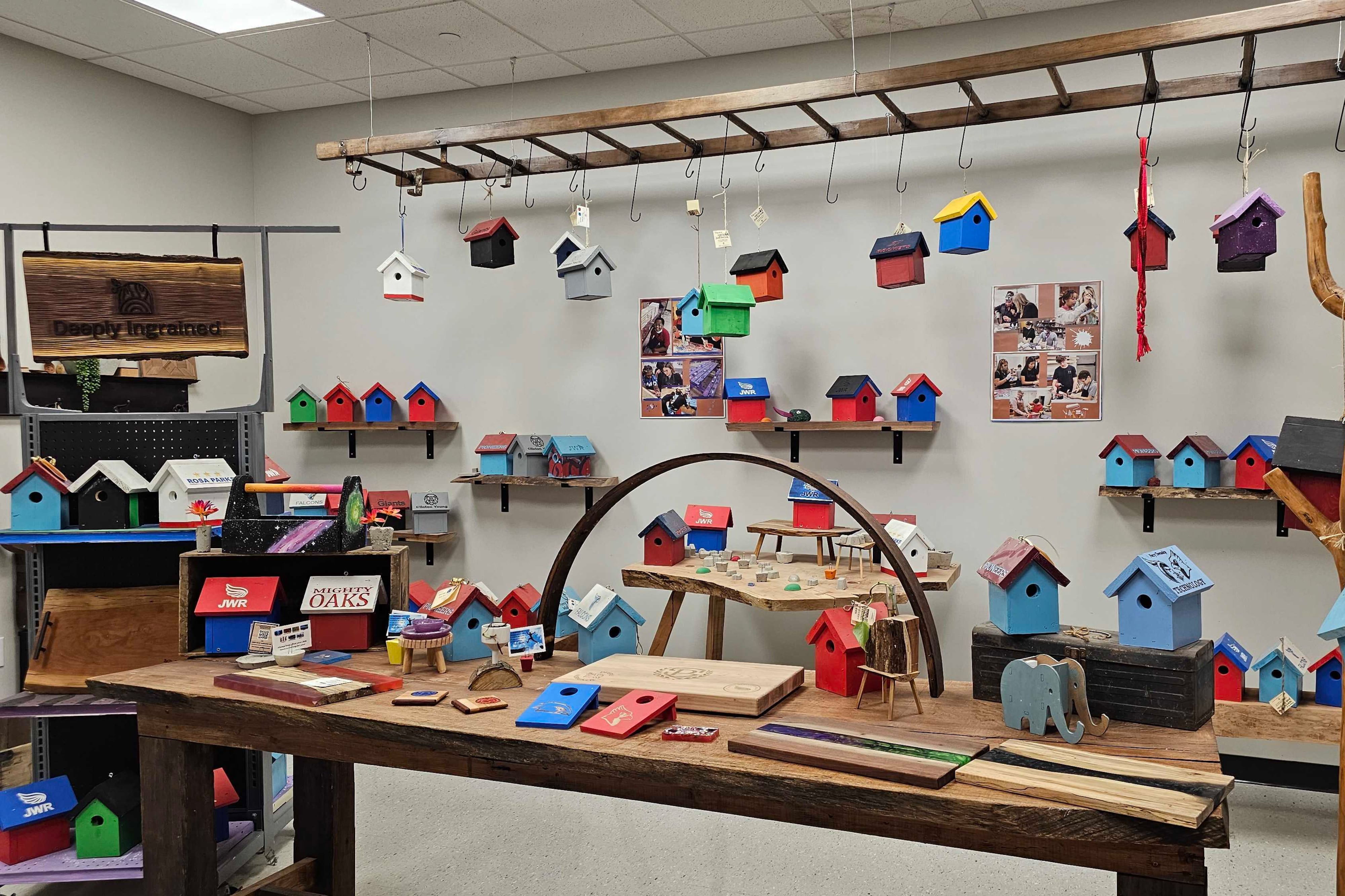 Dozens of multicolored birdhouses are hanging from the ceiling and displayed on shelves and counter space inside of a middle school's woodshop.