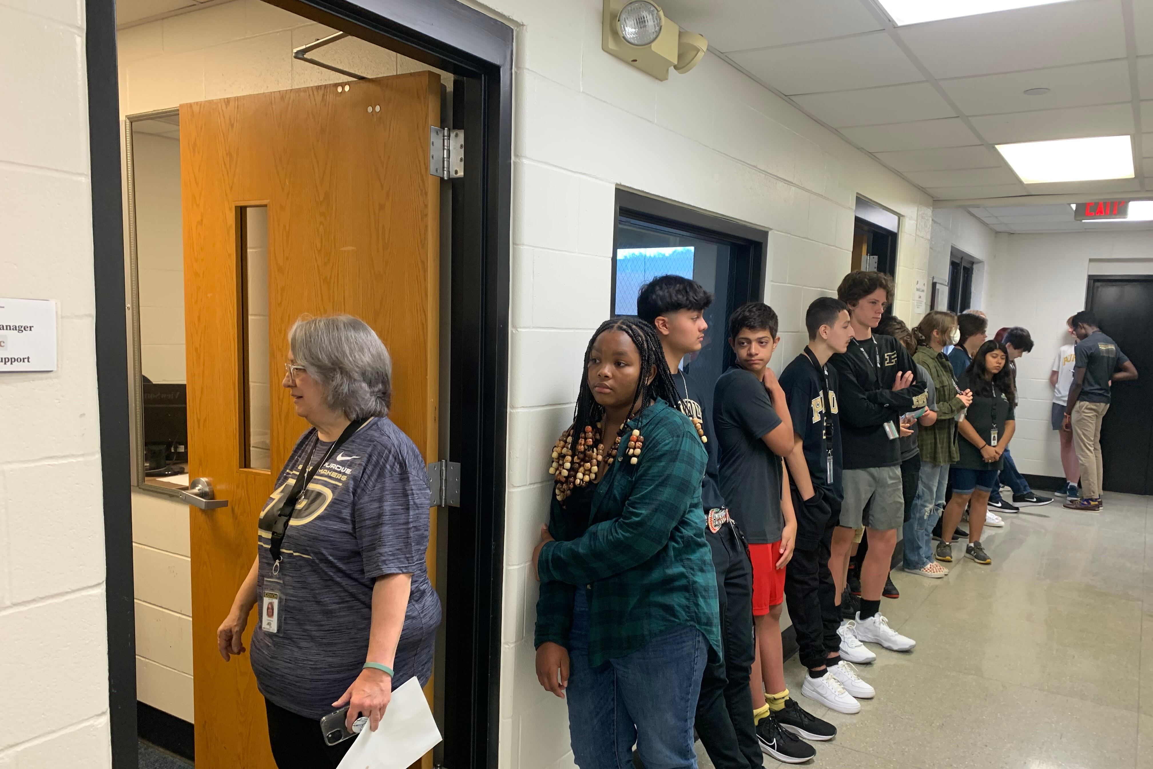 A staff member stands in the doorway next to a long line of high school students.
