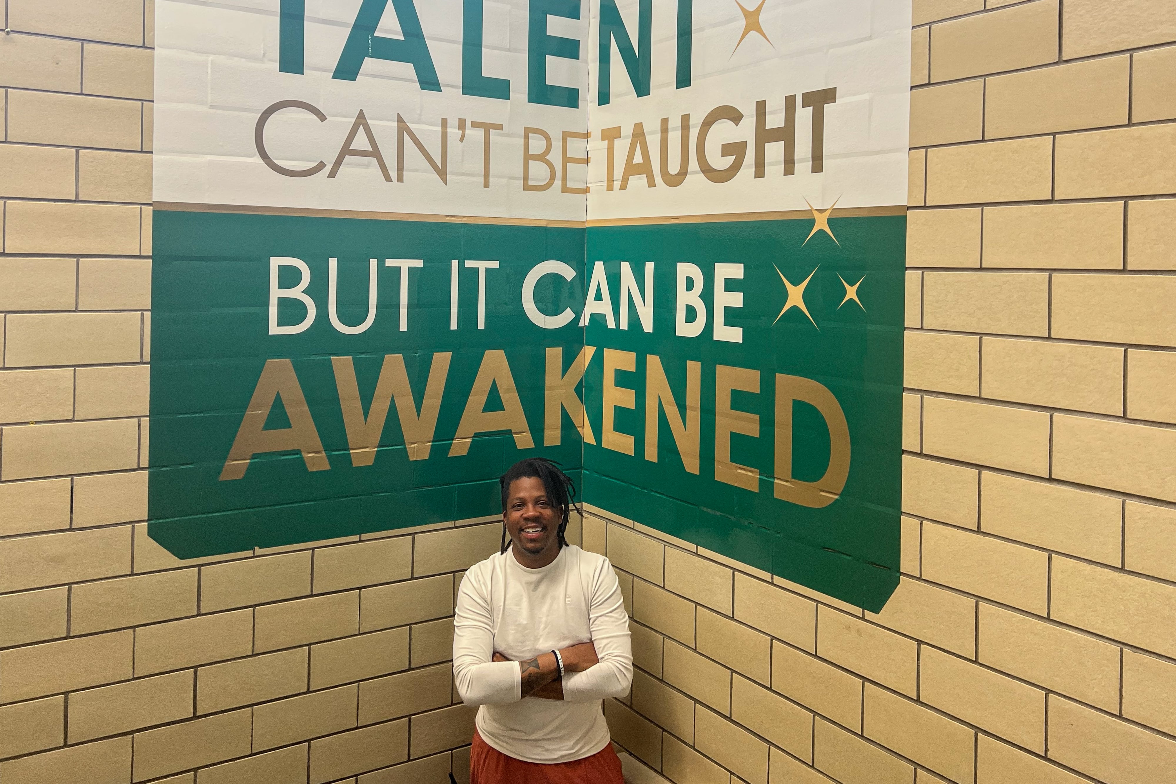 A principal stands under a green and white sign that says “Talent cant’ be taught, but it can be awakened.”