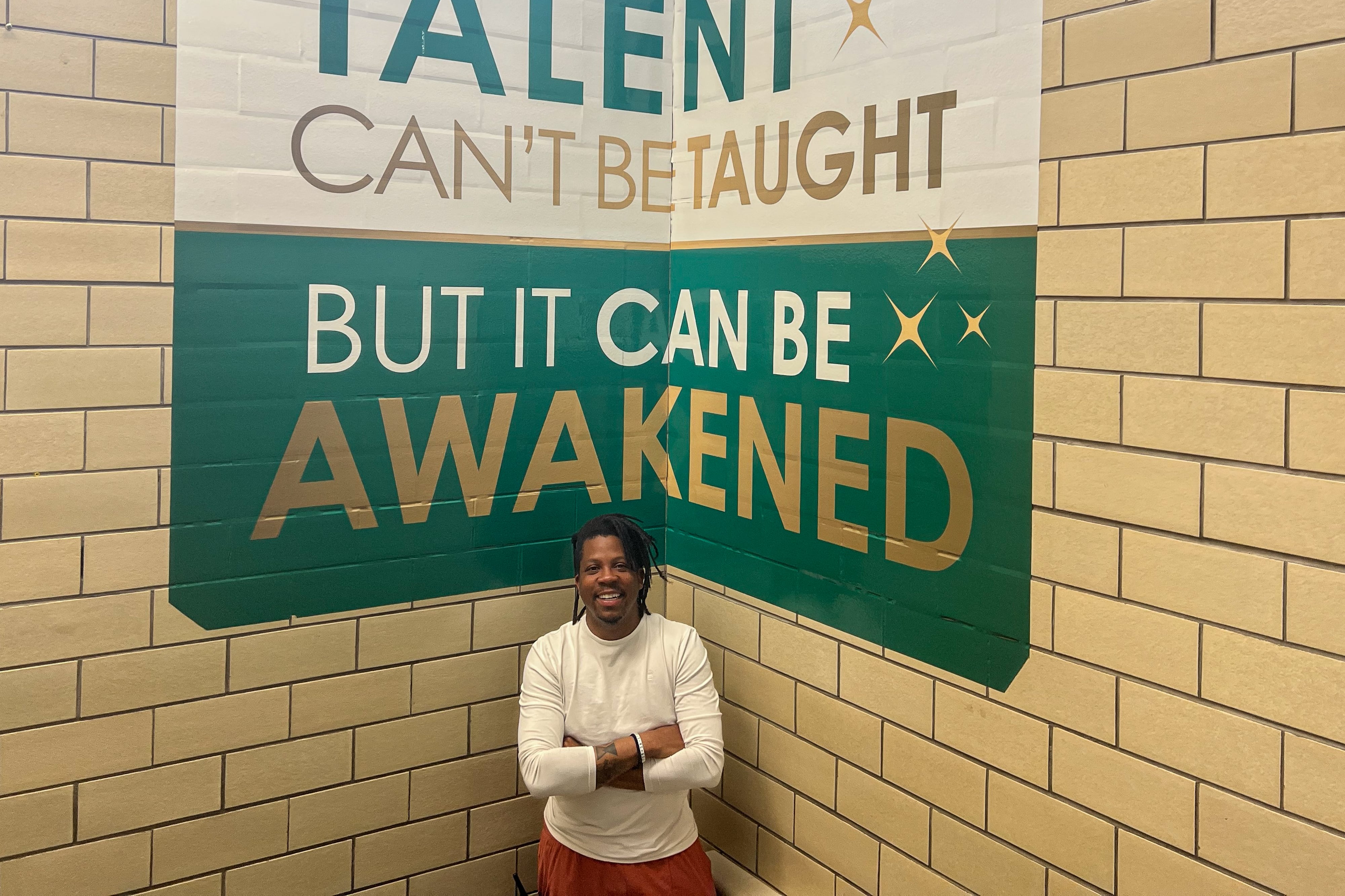 A principal stands under a green and white sign that says “Talent cant’ be taught, but it can be awakened.”