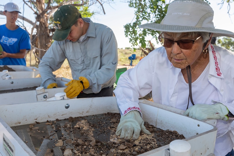 A photograph of two people working with soil at an archaeological dig at Japanese Internment Camp outside on a sunny day.