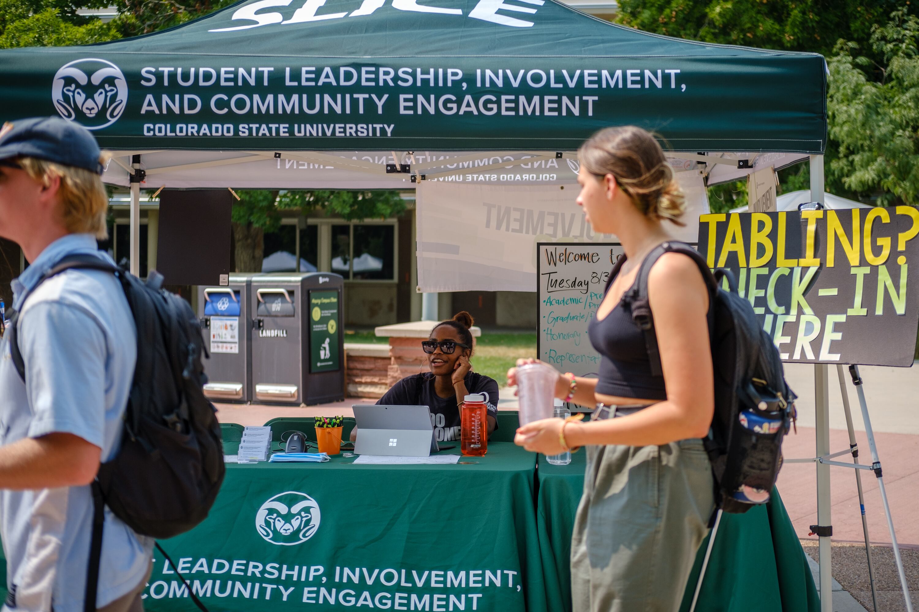 Students walk past a table and canopy advertising Colorado State University’s Student Leadership, Involvement, and Community Engagement during a student involvement fair.