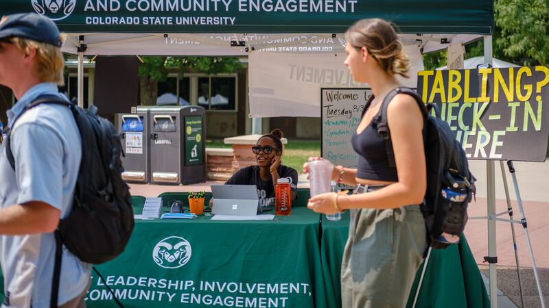 Students walk past a table and canopy advertising Colorado State University’s Student Leadership, Involvement, and Community Engagement during a student involvement fair.