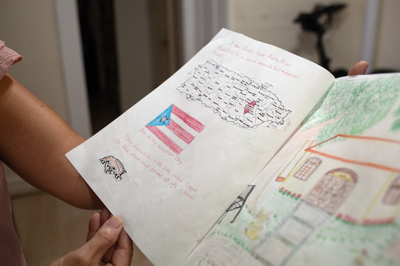 A child holds open a notebook with drawings and writing.