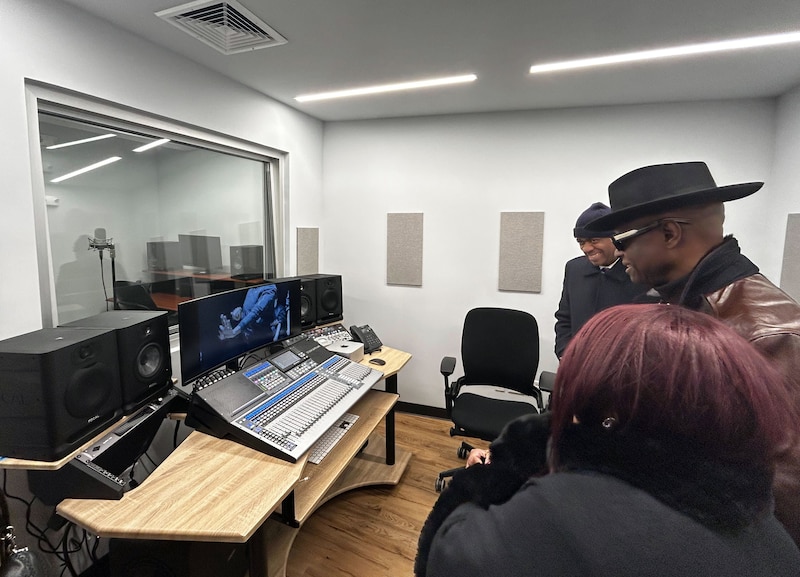 Adults stand next to audio recording equipment in a room.