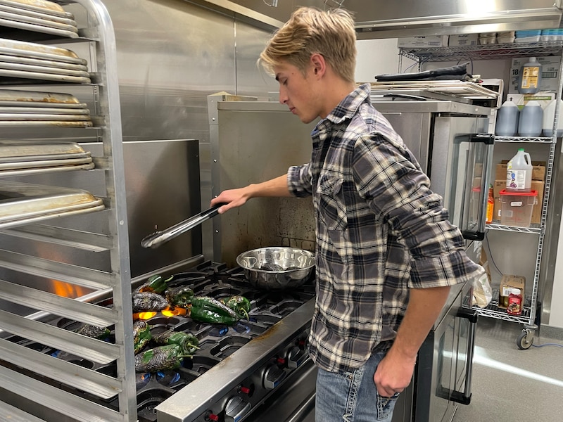 A high school student roasts green chili peppers over a gas stove.